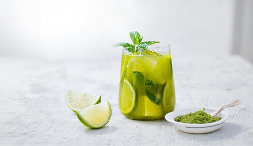 Matcha Mojito: een glas met een Matcha Mojito met limoen en munt en een schaaltje matcha ernaast
